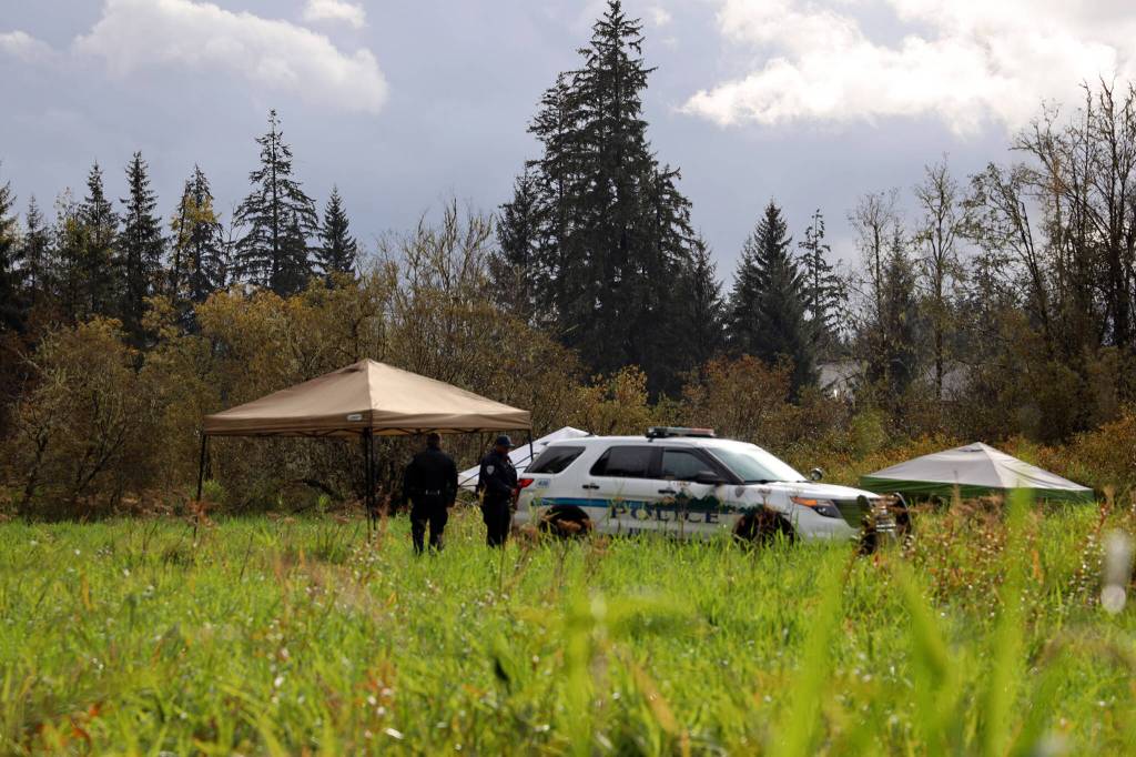 On Thursday morning at the crime scene, JPD Officer Austin Thomas and Officer Taylor Davis walk the fielded area which was blocked off by crime scene tape. Multiple tents and a police vehicle sat in the field where the tape surrounded, another police vehicle sat in a dirt parking area. (Clarise Larson / Juneau Empire)
