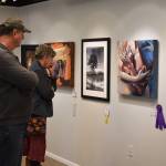 Attendees of the opening reception of the Kenai Art Center Biennial Juried Show look at a wall of art that includes Best of Show winner Cross My Heart, an untitled photograph which won honorable mention, the third place winner Civil Disobedience, and Jurors Choice The Dead Skate, on Thursday, Oct. 6, 2022, at the Kenai Art Center in Kenai, Alaska. (Jake Dye/Peninsula Clarion)
