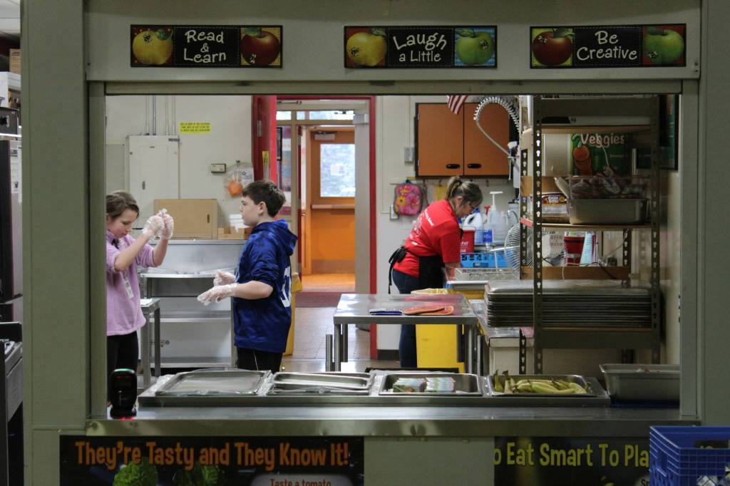 From left: sixth graders Katelynn Albritton and Ford Jacobson assist Kitchen Manager Toni Buchanan in the cafeteria at Sterling Elementary School on Thursday, Nov. 10, 2022, in Sterling, Alaska. (Ashlyn OHara/Peninsula Clarion)