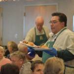 A volunteer from Hilcorp distributes dinners to seniors on Friday, Nov. 18, 2022, at the Area-Wide Senior Dinner at Kenai Seniors Center in Kenai, Alaska. (Jake Dye/Peninsula Clarion)