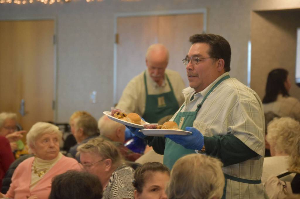 A volunteer from Hilcorp distributes dinners to seniors on Friday, Nov. 18, 2022, at the Area-Wide Senior Dinner at Kenai Seniors Center in Kenai, Alaska. (Jake Dye/Peninsula Clarion)
