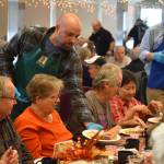 A volunteer from Hilcorp distributes dinners to seniors on Friday, Nov. 18, 2022, at the Area-Wide Senior Dinner at Kenai Seniors Center in Kenai, Alaska. (Jake Dye/Peninsula Clarion)
