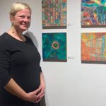 Amy Komar poses with her acrylic on clay board paintings at one the opening of the Mother exhibit showing this month at Bunnell Street Arts Center. (Photo by Christina Whiting)