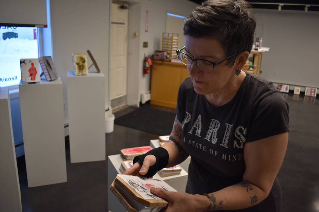 Diane Dunn places a journal that she made and painted by hand, on Tuesday, Jan. 3, 2023, ahead of the opening of 2000 Journals: Filling the Void at the Kenai Art Center in Kenai, Alaska. (Jake Dye/Peninsula Clarion)
