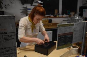 Kelsey Shields applies a Lucys Market sticker to a Cheese of the Month subscription box on Friday, Jan. 6, 2023 at Lucys Market in Soldotna, Alaska. (Jake Dye/Peninsula Clarion)