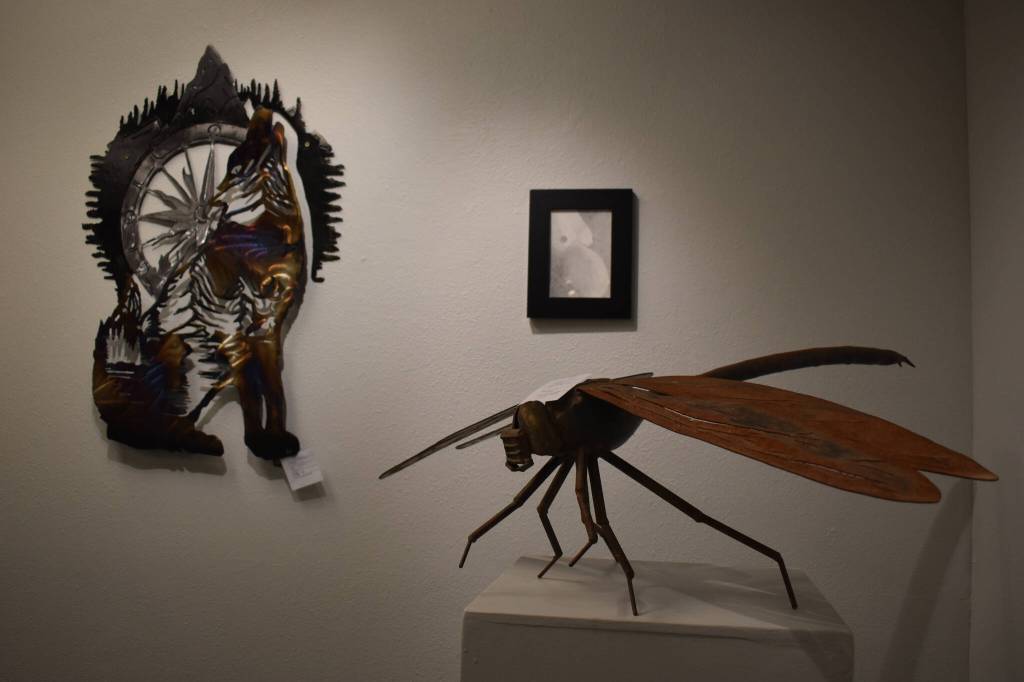 A metal dragonfly sculpted by Dave Emery stands atop a pedestal, two other pieces visible behind it on Tuesday, Jan. 31, 2023, at the Kenai Art Center, in Kenai, Alaska, as part of Metalwork & Play. (Jake Dye/Peninsula Clarion)