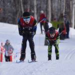 Garrett Briscoe, of Homer, tucks for a downhill, tightly pursued by Colonys Clayton Steer during the boys 4x5-kilometer relay at the ASAA State Nordic Ski Championships at Kincaid Park in Anchorage, Alaska, on Saturday, Feb. 25, 2023. (Jake Dye/Peninsula Clarion)