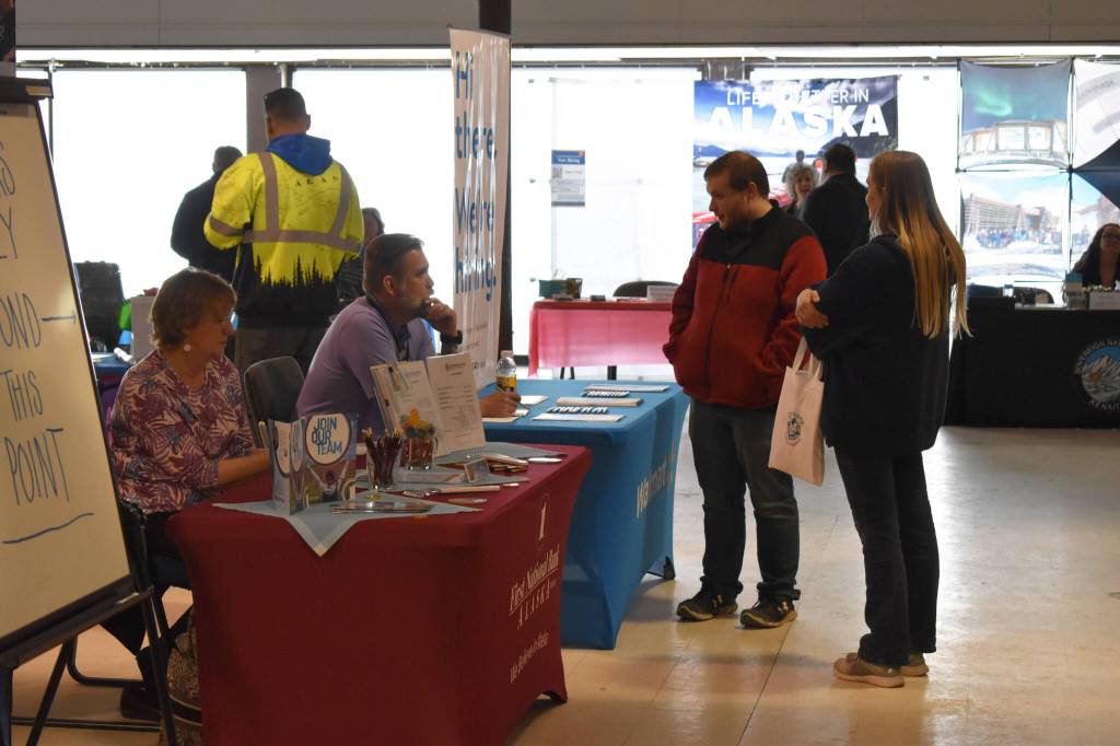 Representatives sitting at a table for First National Bank Alaska speak to a visitor at the Kenai Peninsula Job and Career Fair on Thursday, April 6, 2023, at the Old Carrs Mall in Kenai, Alaska. (Jake Dye/Peninsula Clarion)
