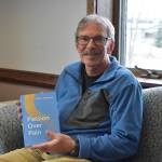 Charlie Stephens sits with a copy of his book, "Passion Over Pain" on Monday, May 1, 2023, in the Peninsula Clarion offices in Kenai, Alaska. (Jake Dye/Peninsula Clarion)