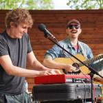 Blackwater Railroad Companys Kyle Comeau performs a piano solo, cheered on by Tyson Davis, during the Levitt AMP Soldotna Music Series on Wednesday, June 7, 2023, at Soldotna Creek Park in Soldotna, Alaska. (Jake Dye/Peninsula Clarion)