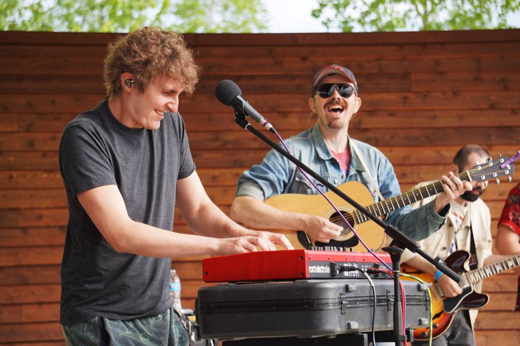 Blackwater Railroad Companys Kyle Comeau performs a piano solo, cheered on by Tyson Davis, during the Levitt AMP Soldotna Music Series on Wednesday, June 7, 2023, at Soldotna Creek Park in Soldotna, Alaska. (Jake Dye/Peninsula Clarion)
