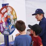 Kids spin a wheel and answer boating questions at a booth run by the U.S. Coast Guard Auxiliary during the Kenai River Festival on Friday, June 9, 2023, at Soldotna Creek Park in Soldotna, Alaska. (Jake Dye/Peninsula Clarion)