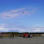 A plane flies overhead as attendees view other planes displayed at the Kenai Peninsula Air Fair on Saturday, June 10, 2023, at the Kenai Municipal Airport in Kenai, Alaska. (Jake Dye/Peninsula Clarion)