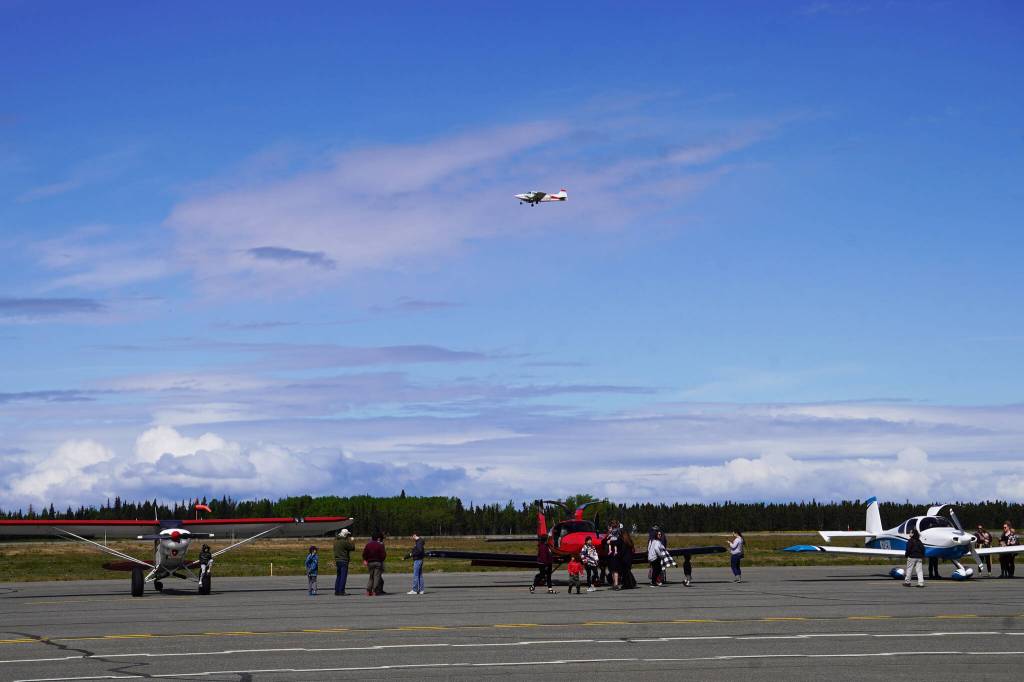 A plane flies overhead as attendees view other planes displayed at the Kenai Peninsula Air Fair on Saturday, June 10, 2023, at the Kenai Municipal Airport in Kenai, Alaska. (Jake Dye/Peninsula Clarion)