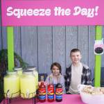 Ellie and Elias Ritter run Squeeze the Day in front of Odies Deli in Soldotna, Alaska, on Lemonade Day, Saturday, June 10, 2023. (Jake Dye/Peninsula Clarion)