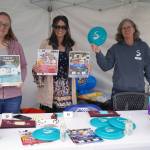 Kenai Peninsula Food Bank Administrative Assistant Claire Jones and Donations and Communications Manager Lilly Murray stand with Soldotna Vice Mayor Lisa Parker as they fundraise for the King of the River Food Drive at the Wednesday Market in Soldotna Creek Park in Soldotna, Alaska, on Wednesday, June 28, 2023. (Jake Dye/Peninsula Clarion)