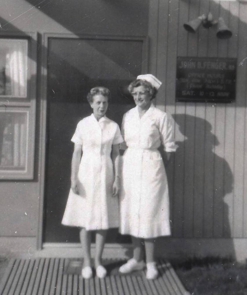 Registered nurses Kay Cowles (wife of Homers first mayor) and Wilma Cowgill pose in the sunshine outside of Dr. John Fengers clinic at the corner of Hohe and Cityview, east of the hospital in Homer.