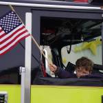 A boy waves a flag from the passenger seat of a Nikiski Fire Department truck as the Fourth of July Parade moves down South Willow Street in Kenai, Alaska on Tuesday, July 4, 2023. (Jake Dye/Peninsula Clarion)