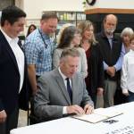 Gov. Mike Dunleavy (sitting) signs House Bill 56, exempting Alaska veterinarians from the states prescription drug monitoring program, next to bill sponsor Rep. Justin Ruffridge (left) at a bill signing event at Twin Cities Veterinary Clinic on Thursday, July 6, 2023 in Soldotna, Alaska. (Ashlyn OHara/Peninsula Clarion)