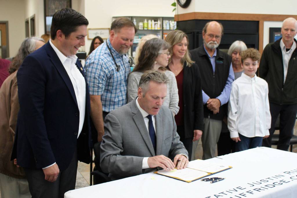Gov. Mike Dunleavy (sitting) signs House Bill 56, exempting Alaska veterinarians from the states prescription drug monitoring program, next to bill sponsor Rep. Justin Ruffridge (left) at a bill signing event at Twin Cities Veterinary Clinic on Thursday, July 6, 2023 in Soldotna, Alaska. (Ashlyn OHara/Peninsula Clarion)