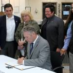 Gov. Mike Dunleavy (sitting) signs House Bill 112, clarifying the power and duties of the Alaska Board of Pharmacy, next to bill sponsor Rep. Justin Ruffridge (left) at a bill signing event at Twin Cities Veterinary Clinic on Thursday, July 6, 2023 in Soldotna, Alaska. (Ashlyn OHara/Peninsula Clarion)