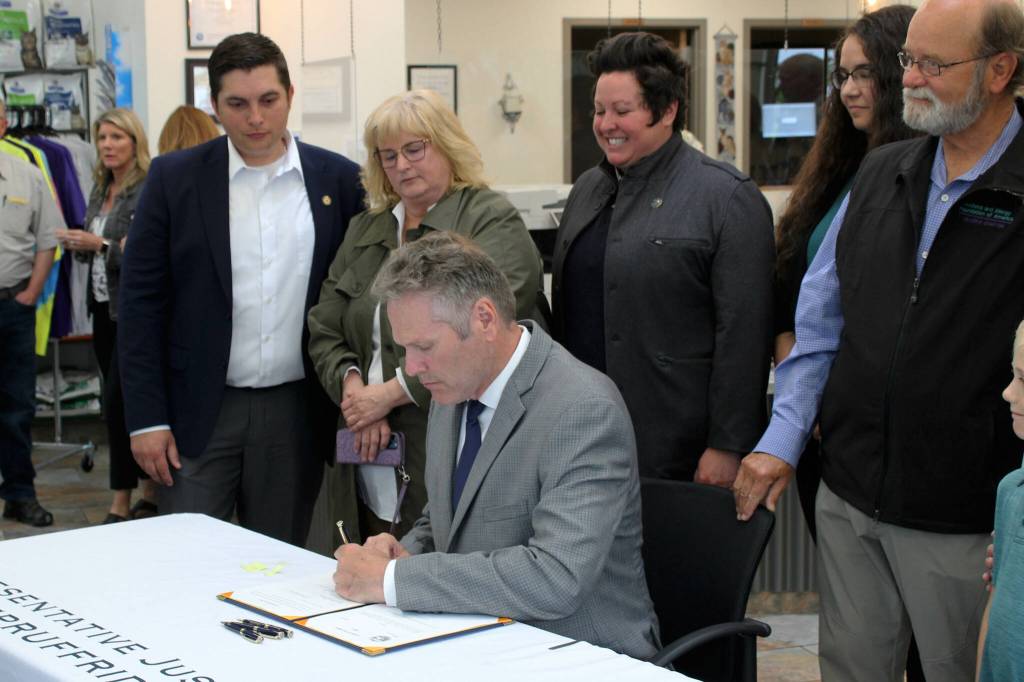 Gov. Mike Dunleavy (sitting) signs House Bill 112, clarifying the power and duties of the Alaska Board of Pharmacy, next to bill sponsor Rep. Justin Ruffridge (left) at a bill signing event at Twin Cities Veterinary Clinic on Thursday, July 6, 2023 in Soldotna, Alaska. (Ashlyn OHara/Peninsula Clarion)