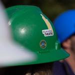 The Triumvirate Theatre logo is stickered onto a hard hat worn by an actor at the ceremonial groundbreaking for the future home of Triumvirate Theatre at Daubenspeck Family Park in Kenai, Alaska, on Saturday, Aug. 19, 2023. (Jake Dye/Peninsula Clarion)