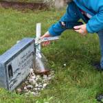 Victoria Askin rights a cross at the headstone of Nels C. Juliussen in the Kenai Cemetery as part of a city imaging project on Friday, Sept. 8, 2023, in Kenai, Alaska. (Ashlyn OHara/Peninsula Clarion)