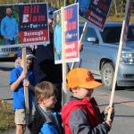 From left: William, Andrew and James Elam wave signs for their dad, Kenai Peninsula Borough Assembly candidate Bill Elam, on election day on Tuesday, Oct. 3, 2023, in Soldotna, Alaska. (Ashlyn OHara/Peninsula Clarion)
