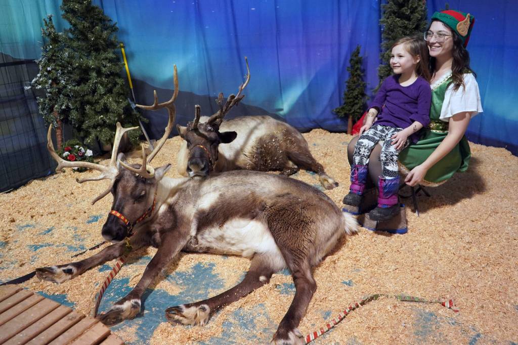 Jenna Bedford, of Kenai Reindeer Farm, sits next to her reindeer with Juliana Bedford during the Fourth Annual Holiday Cheer Christmas Bazaar at the Old Carrs Mall in Kenai, Alaska, on Saturday, Dec. 9, 2023. (Jake Dye/Peninsula Clarion)