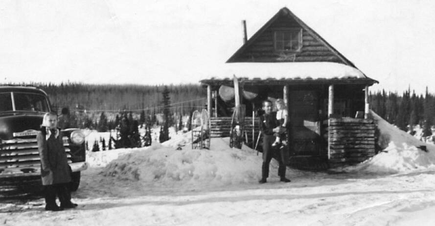 Ray Sandstrom photo courtesy of the KPC historical photo archive
Floyd Pappy Keeler, standing in 1951 in front of his cabin on the homestead of his son Jack, is holding a girl who is likely Barbara Sandstrom, while her sister Rhoda, standing by a truck, looks on.