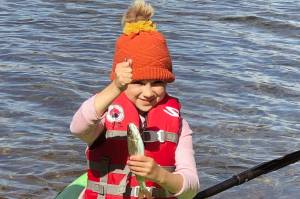 If you teach a kid to fish, she will feed you a trout breakfast every morning of the campout. This proved true for this girl, who holds up a rainbow trout while sitting on a kayak. (Photo by Leah Eskelin)