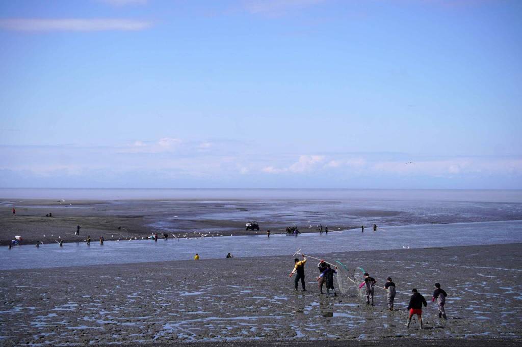 Fishers carry nets across a muddy beach during the opening day of the personal use dipnet fishery at the mouth of the Kasilof River in Alaska, on Tuesday, June 25, 2024. (Jake Dye/Peninsula Clarion)