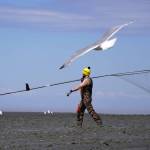 A fisher carries his net across a muddy beach during the opening day of the personal use dipnet fishery at the mouth of the Kasilof River in Alaska, on Tuesday, June 25, 2024. (Jake Dye/Peninsula Clarion)