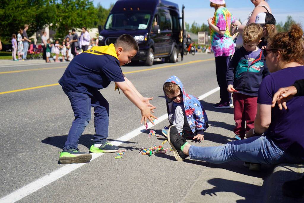 A boy scout deposits a bounty of candy at the feet of children while walking with the 67th Annual Soldotna Progress Days Parade down Binkley Street in Soldotna, Alaska, on Saturday, July 27, 2024. (Jake Dye/Peninsula Clarion)