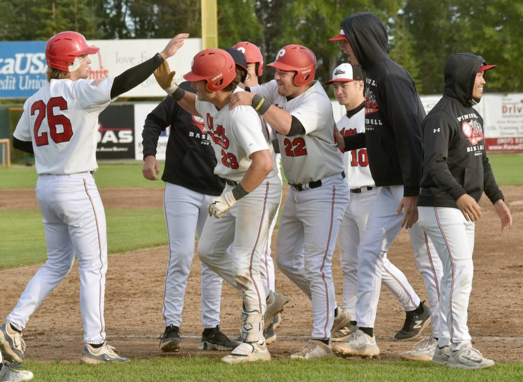 Peninsula Oilers catcher Braden Smith (23) gets congratulations from Cody New (26) on Monday, July 29, 2024, at Coral Seymour Memorial Park in Kenai, Alaska. Smith drove in New for the game-winning run in the bottom of the 10th inning. (Photo by Jeff Helminiak/Peninsula Clarion)