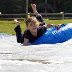 Children participate in a water slide during a celebration of the 50th anniversary of North Peninsula Recreation Service Area at the Nikiski Pool in Nikiski, Alaska, on Saturday, Aug. 3, 2024. (Jake Dye/Peninsula Clarion)