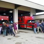 Kenai Fire Department staff and other attendees push a new ambulance into the garage at the Kenai Public Safety Building in Kenai, Alaska, on Saturday, Aug. 17, 2024. (Jake Dye/Peninsula Clarion)