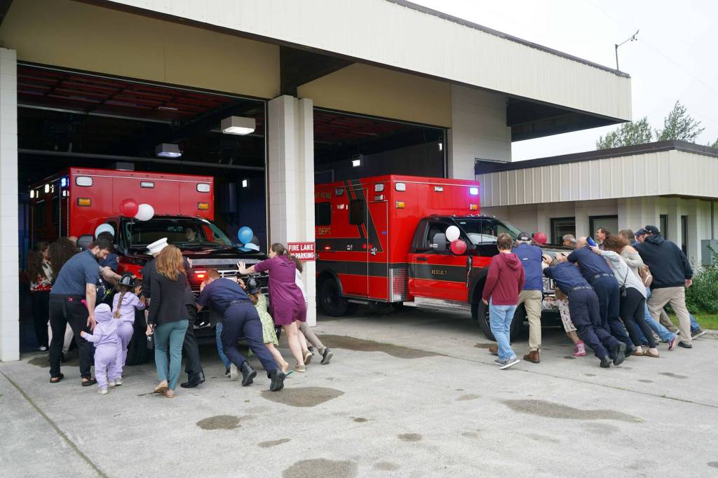 Kenai Fire Department staff and other attendees push a new ambulance into the garage at the Kenai Public Safety Building in Kenai, Alaska, on Saturday, Aug. 17, 2024. (Jake Dye/Peninsula Clarion)