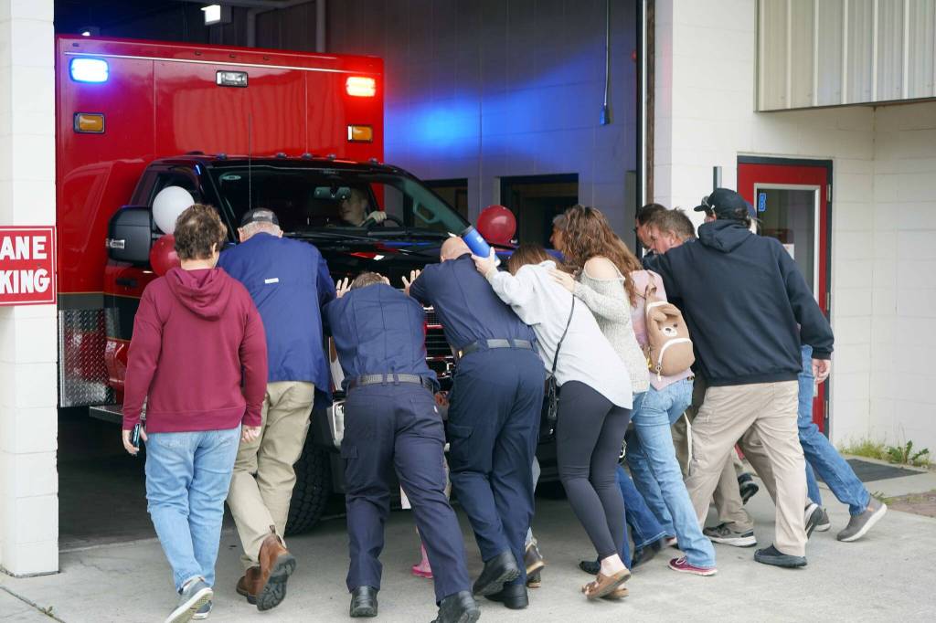 Kenai Fire Department staff and other attendees push a new ambulance into the garage at the Kenai Public Safety Building in Kenai, Alaska, on Saturday, Aug. 17, 2024. (Jake Dye/Peninsula Clarion)