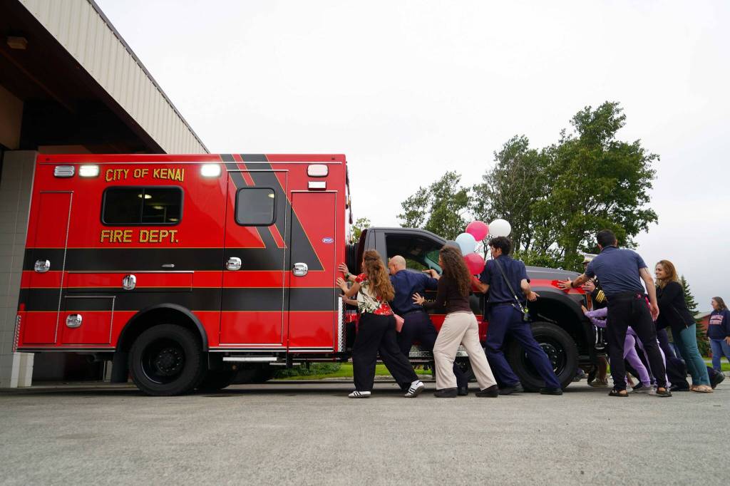 Kenai Fire Department staff and other attendees push a new ambulance into the garage at the Kenai Public Safety Building in Kenai, Alaska, on Saturday, Aug. 17, 2024. (Jake Dye/Peninsula Clarion)