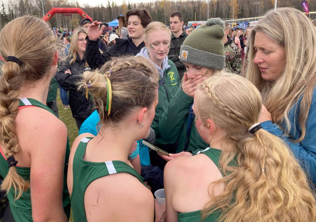 Seward cross-country head coach Rachel Dow looks at results on her phone while her team huddles around her at the state cross-country running meet on Saturday, Oct. 5, 2024, at Bartlett High School in Anchorage, Alaska. The Seahawks won a third straight Division II girls title. (Photo by Jeff Helminiak/Peninsula Clarion)