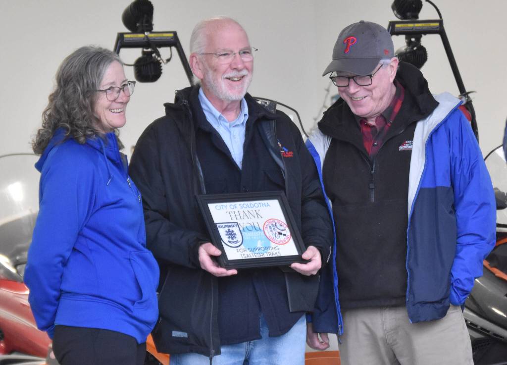 Pat King (right), chair of the Tsalteshi Trails Association Board of Directors, presents Lisa Parker of the Soldotna City Council and Soldotna Mayor Paul Whitney with a certificate of appreciation at a winter kick-off and open house event to celebrate a new trail system maintenance shed Saturday, Oct. 12, 2024, just outside of Soldotna, Alaska. (Photo by Jeff Helminiak/Peninsula Clarion)