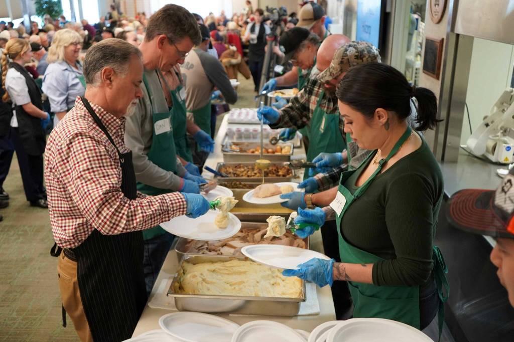 Kenai Peninsula Borough Mayor Peter Micciche and Hilcorp volunteers prepare plates for delivery to tables during the Hilcorp Areawide Senior Thanksgiving Luncheon in the Kenai Senior Center banquet hall in Kenai, Alaska, on Friday, Nov. 22, 2024. (Jake Dye/Peninsula Clarion)