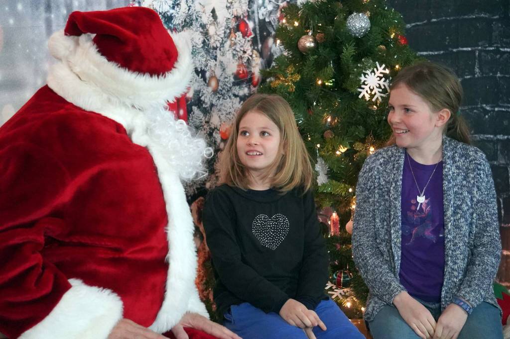 Santa Claus greets Willow and Marigold Dabill during Christmas Comes to Kenai at the Kenai Chamber of Commerce and Visitor Center in Kenai, Alaska, on Friday, Nov. 29, 2024. (Jake Dye/Peninsula Clarion)