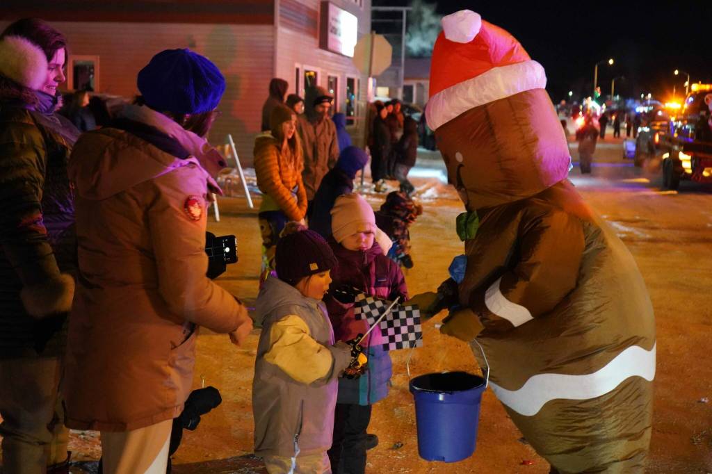 A gingerbread man passes out racing flags to children on behalf of the Kenai Peninsula Ice Racing Association on Frontage Street in Kenai, Alaska, as part of the Electric Lights Parade on Friday, Nov. 29, 2024. (Jake Dye/Peninsula Clarion)