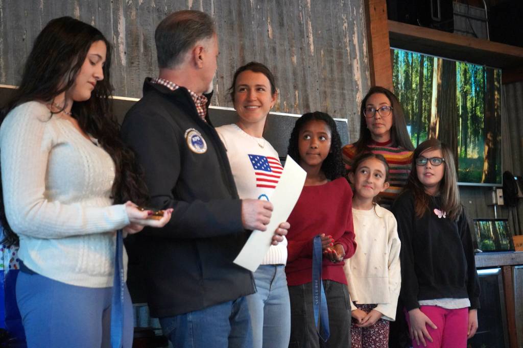 Kenai Peninsula Borough Mayor Peter Micciche is joined by his family as he gives a mayoral proclamation to Kristen Faulkner in recognition of her two gold medal wins at the Paris 2024 Olympics during a meet and greet hosted by the Kenai and Soldotna chambers of commerce at the Cannery Lodge in Kenai, Alaska, on Saturday, Dec. 28, 2024. (Jake Dye/Peninsula Clarion)