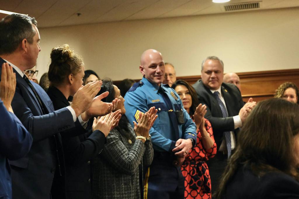 Alaska State Trooper Sgt. Jared Noll, center, is honored during Gov. Mike Dunleavys State of the State speech on Tuesday, Jan. 28, 2025, at the Alaska State Capitol. He is surrounded by members of Dunleavys Cabinet and other guests, including Dunleavys wife, Rose Dunleavy, third from left. (Klas Stolpe/Juneau Empire)