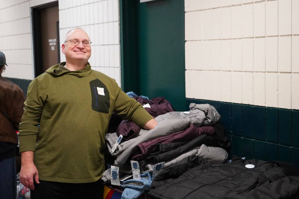 A volunteer stands with a pile of coats available to participants of the 14th Annual Project Homeless Connect at the Soldotna Regional Sports Complex in Soldotna, Alaska, on Tuesday, Jan. 28, 2025. (Jake Dye/Peninsula Clarion)