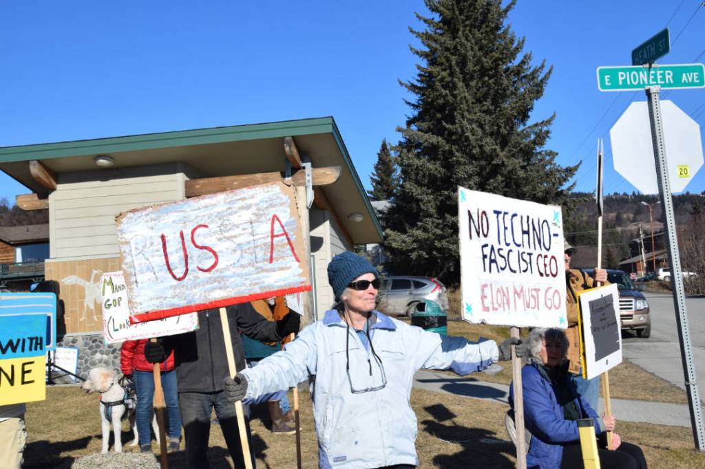 A community member holds up protest signs during the Stand for Democracy Rally on International Womens Day, March 8, 2025, at WKFL Park in Homer, Alaska. (Chloe Pleznac/Homer News)